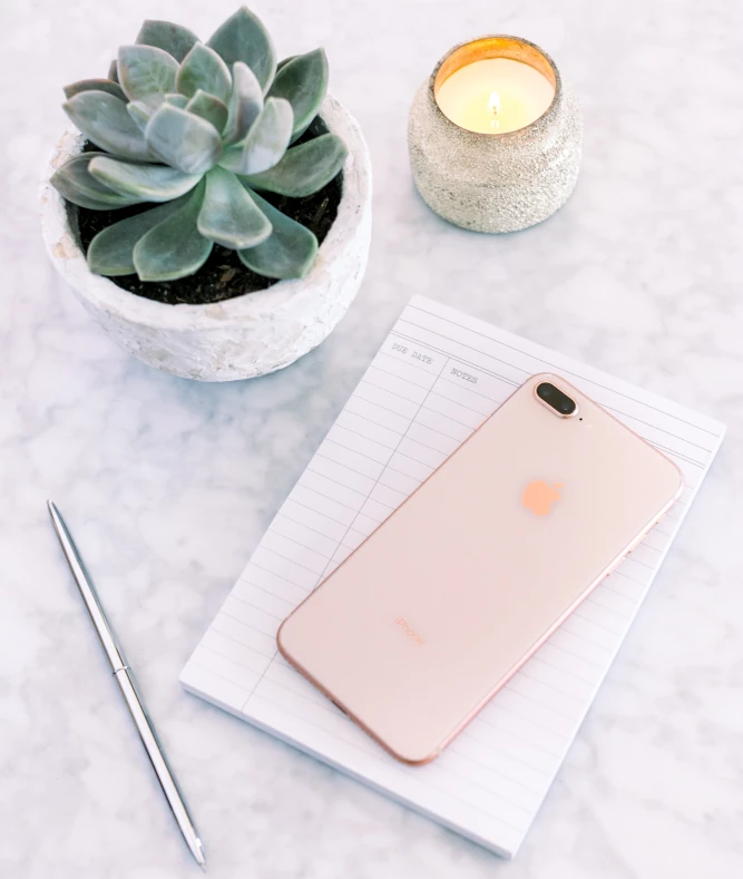 Mobile phone resting on top of notepad with plant candle next to them