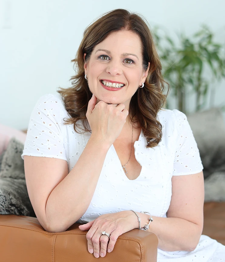 Rachel smiling in white dress sitting on couch